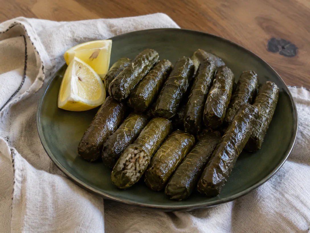 Yeşil seramik tabakta ince sarılmış zeytinyağlı yaprak sarma ve limon dilimleri